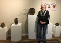 Picture of me  in front of 5 pedestals with my pottery on top. A sign on the wall behind reads 