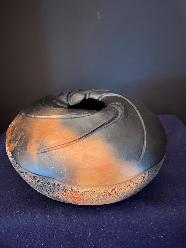 Small rounded pot, textured on the botton, with carvings on top. Burnished and pit fired to bring out the clay's natural orange coloring, with swirls of black smoke.