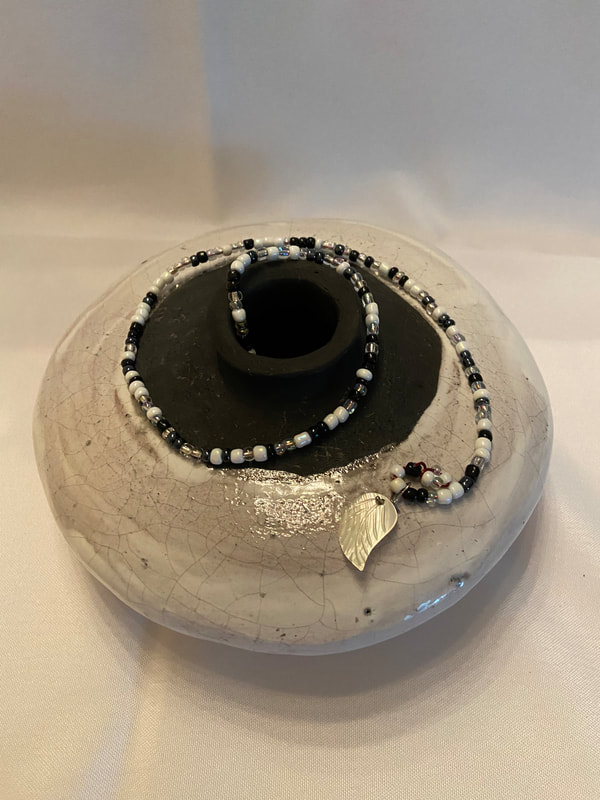 Small vase glazed with white crackle raku glaze, then raku fired and embellished with black and white beads that twirl around the neck.