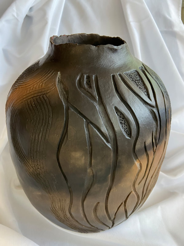 Mica clay formed into small vase with floral accent moving from bottom to top. Burnished and pit fired.